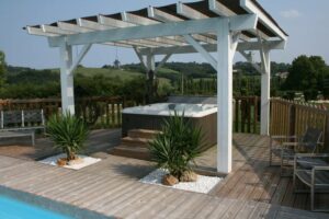 A hot tub under a white pergola hot tub enclosure with plants